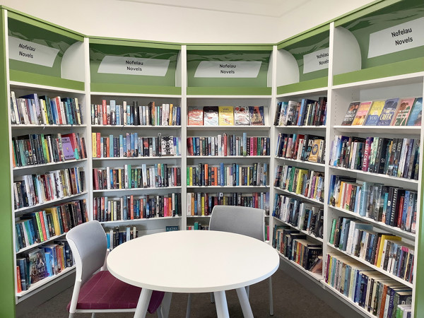 White circular table with grey chairs surrounded by colourful book displays in a novel section at Uwchaled Library