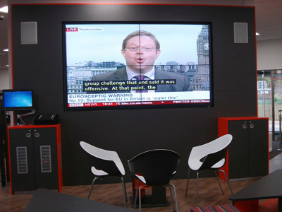 Large screen displaying a news broadcast with modern seating in a digital engagement area at Brackenhurst Campus Library