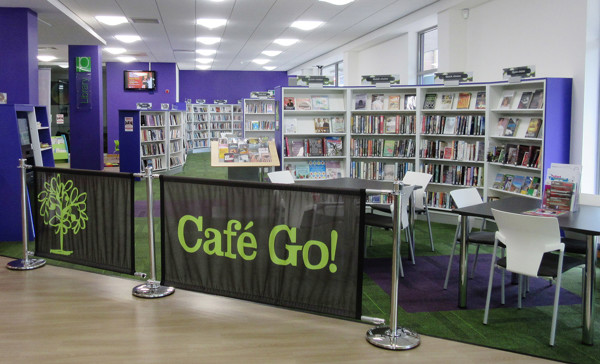 Bright green signage for Café Go! beside study tables and browsing shelves in a public library browsing area at The Place Library & Theatre, Telford