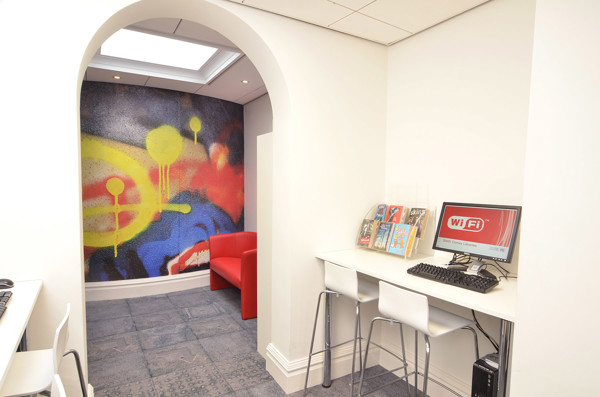 Red sofa and computer workstation beside a colourful mural in a young people's browsing space at Llandudno Library