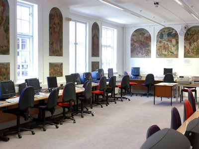 Computers with ergonomic chairs and mural-adorned walls in a study area at Wimbledon Library