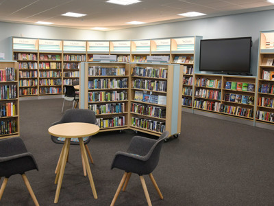 Two grey upholstered chairs and a circular table in a young readers' browsing space with book displays at Birtley Library