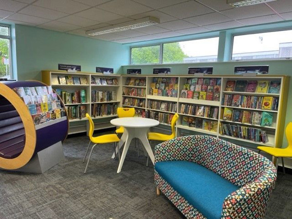 Colourful patterned sofa and yellow chairs around a white table in a children's reading area at Abergele Library