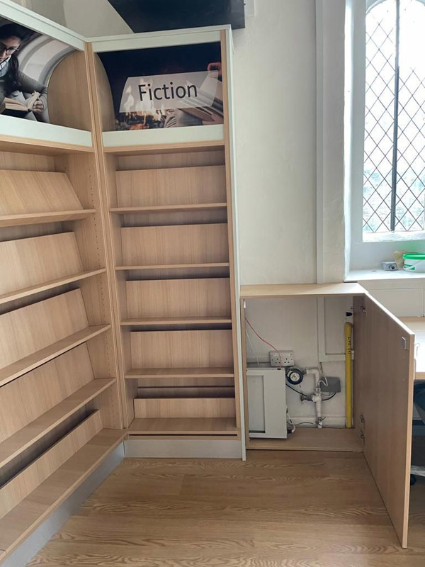 Custom shelving designed around heating pipes in a library shelving unit at Bampton Library