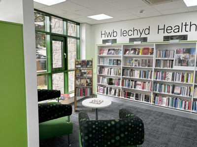 Green upholstered chairs with polka dots beside a book display in a health and wellbeing zone at Llanrwst Library