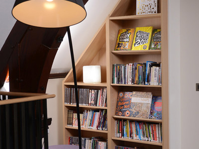 Angular wooden shelving filled with books beside a floor lamp in a reading nook at Kingham Hill Library