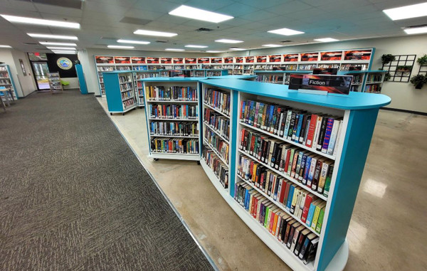 Curved white shelving units filled with fiction titles in a browsing area at Riviera Beach Public Library, Florida