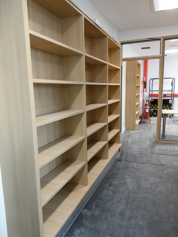 Light wood shelving units with multiple compartments in a newly installed library space at Brecon Library
