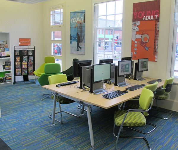 Green upholstered chairs and a collaborative work table with computers in a young readers' browsing space at West Bridgford Library