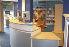Library help desk design — modern welcome counter and staff pod in a public library interior
