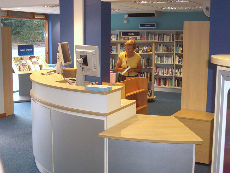 Curved help desk with a computer and wooden shelving in the background at Horsley Library