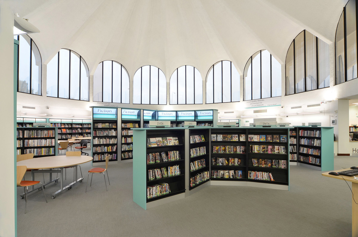 Curved shelving units filled with books and a study table in a light-filled reading area at Fullwell Cross Library