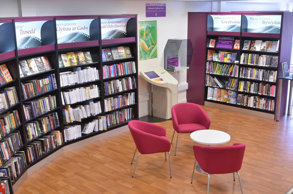 Pink lounge chairs and a round table in a public library browsing area featuring colourful book displays at Risca Palace Library
