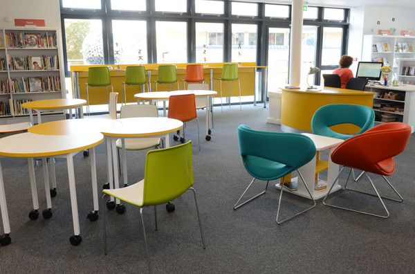 Bright orange, green, and blue chairs around white study tables in a young readers' browsing space at King Edward's School