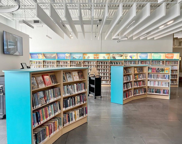 Curved wooden book displays in a light-filled browsing area featuring colourful book covers at Holly Branch, Barrie Public Library, Ontario