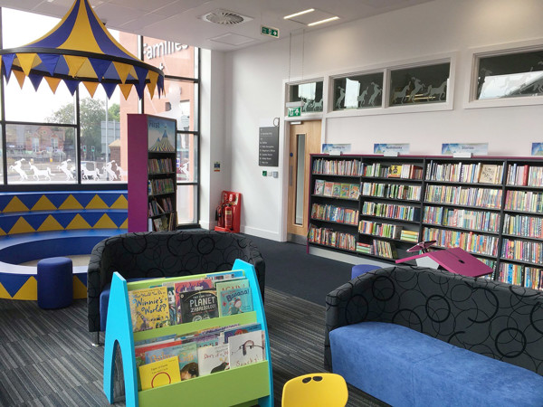 Colourful seating areas with a blue sofa and a green kinderbox book bin in a children's reading area at Newcastle Under Lyme Library