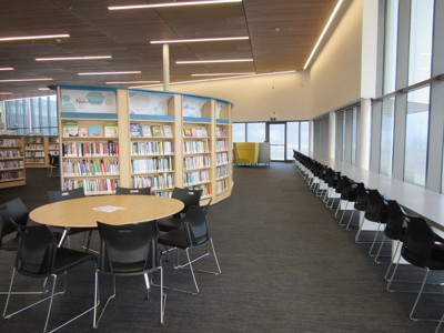 Curved face-out book displays and round study tables in a bright open-plan library floor at Sherwood Library