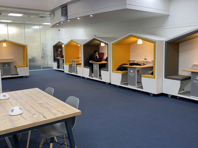 Individual work pods with yellow seating and wooden tables in a collaborative workspace at Shoreditch Library