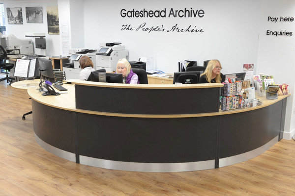 Curved wooden help desk with staff assisting customers at Gateshead Archive at Gateshead Library