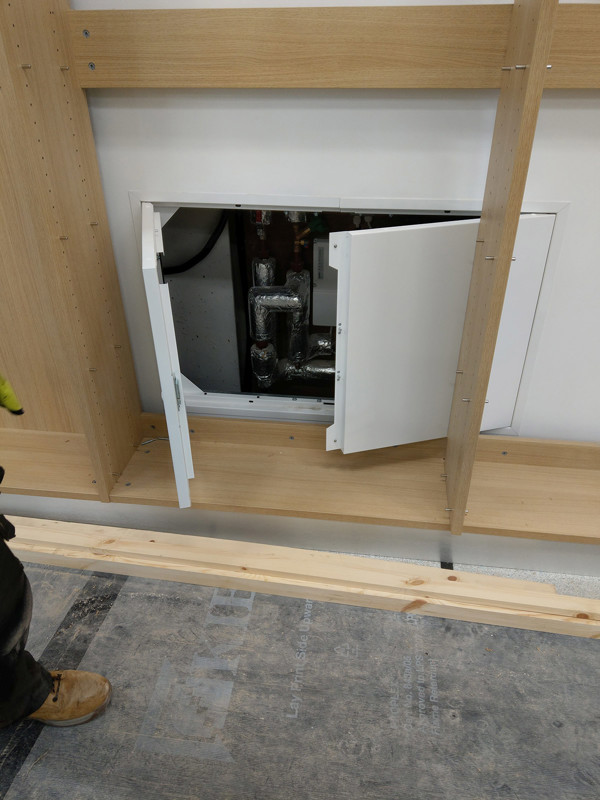 Access panel with doors opened revealing plumbing behind custom shelving at Brecon Library