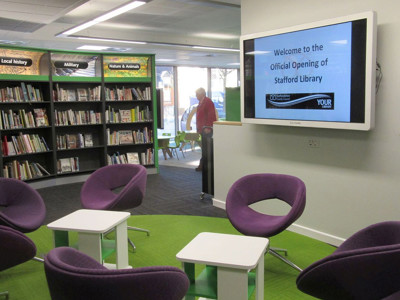 Purple lounge chairs arranged around white side tables in a digital presentation area at Stafford Library