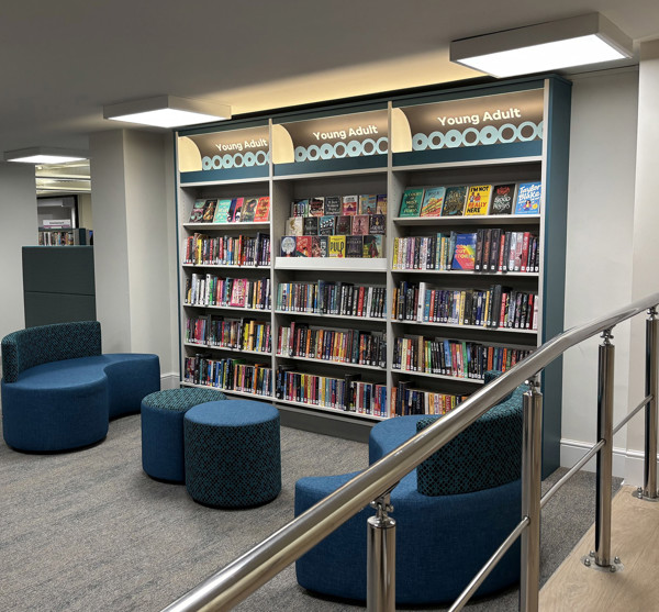 Blue upholstered seating and circular stools in a young adult browsing area with graphic book displays at Sale Library