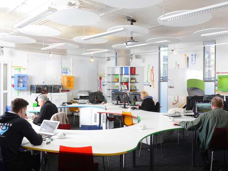 Curved white tables with colourful storage units and computer stations in a collaborative workspace at Stafford Innovation Suite