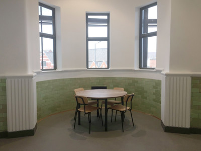 Round wooden table with black chairs in a study area featuring green tiled walls at Danum Library