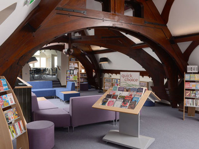 Curved wooden beams and purple upholstered seating create a unique reading area with face-out book displays at Kingham Hill School