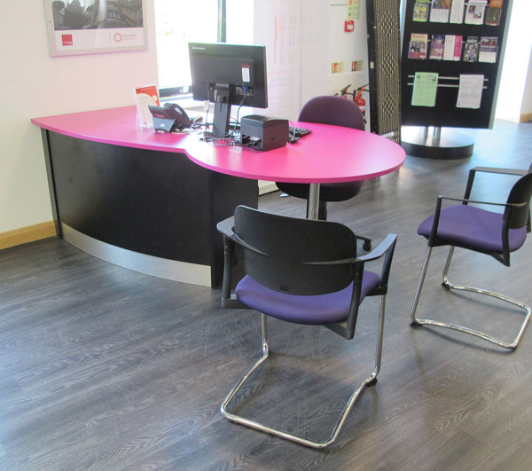 Curved pink reception desk with a computer and black chairs in the advice area at Wellington Library