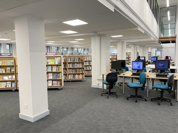 Study tables and computer stations beside browser shelving in an open-plan library space at Islington Central Library