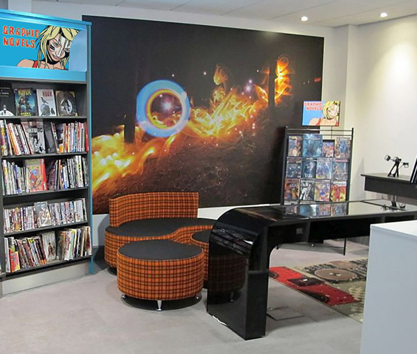 Curved orange and black seating beside a graphic novels display and a large mural at Bridgend Library