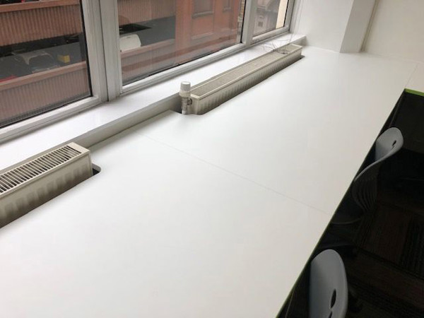 Long white study tables beside large windows with heating units at INTO Manchester Library