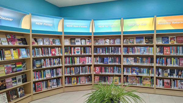 Curved wooden shelving displaying a diverse collection of books with colourful signage at Painswick Branch