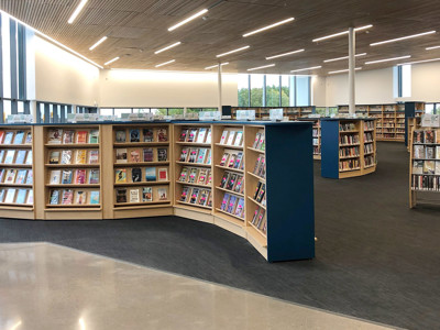 Curved wooden bookcases filled with face-out titles in a public library browsing area at Sherwood Library