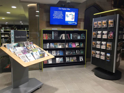 Face-out book displays and a digital screen showcasing library services in a browsing area at Lichfield Library