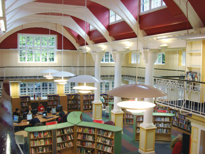 Curved green circulation desk and modern pendant lights in a spacious reading area at Sefton Park Library