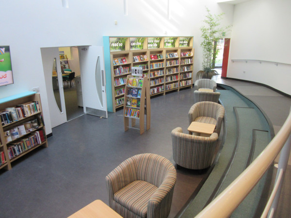 Striped lounge chairs and wooden side tables in a reading lounge beside browsing shelves at Wrekin College Library