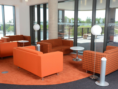 Orange upholstered sofas and round side tables on a carpeted seating area at Southwater Library