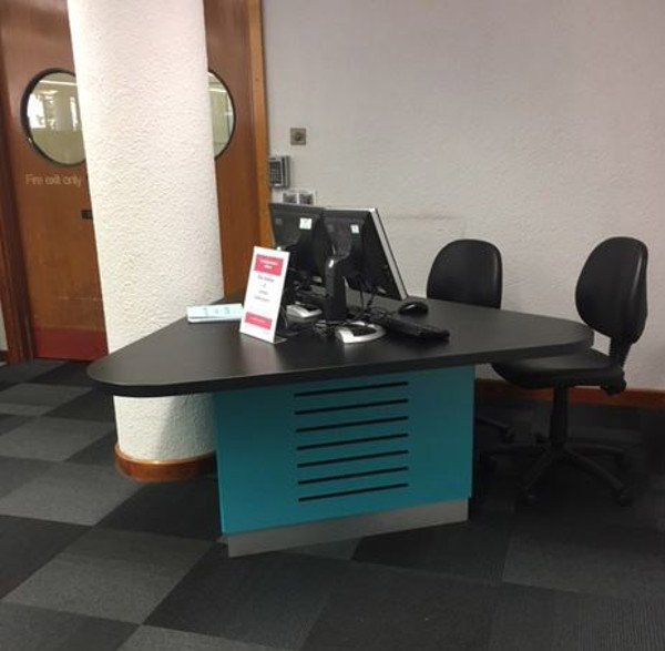 Curved black desk with a computer and advice signage in a contact area at Redbridge Central Library