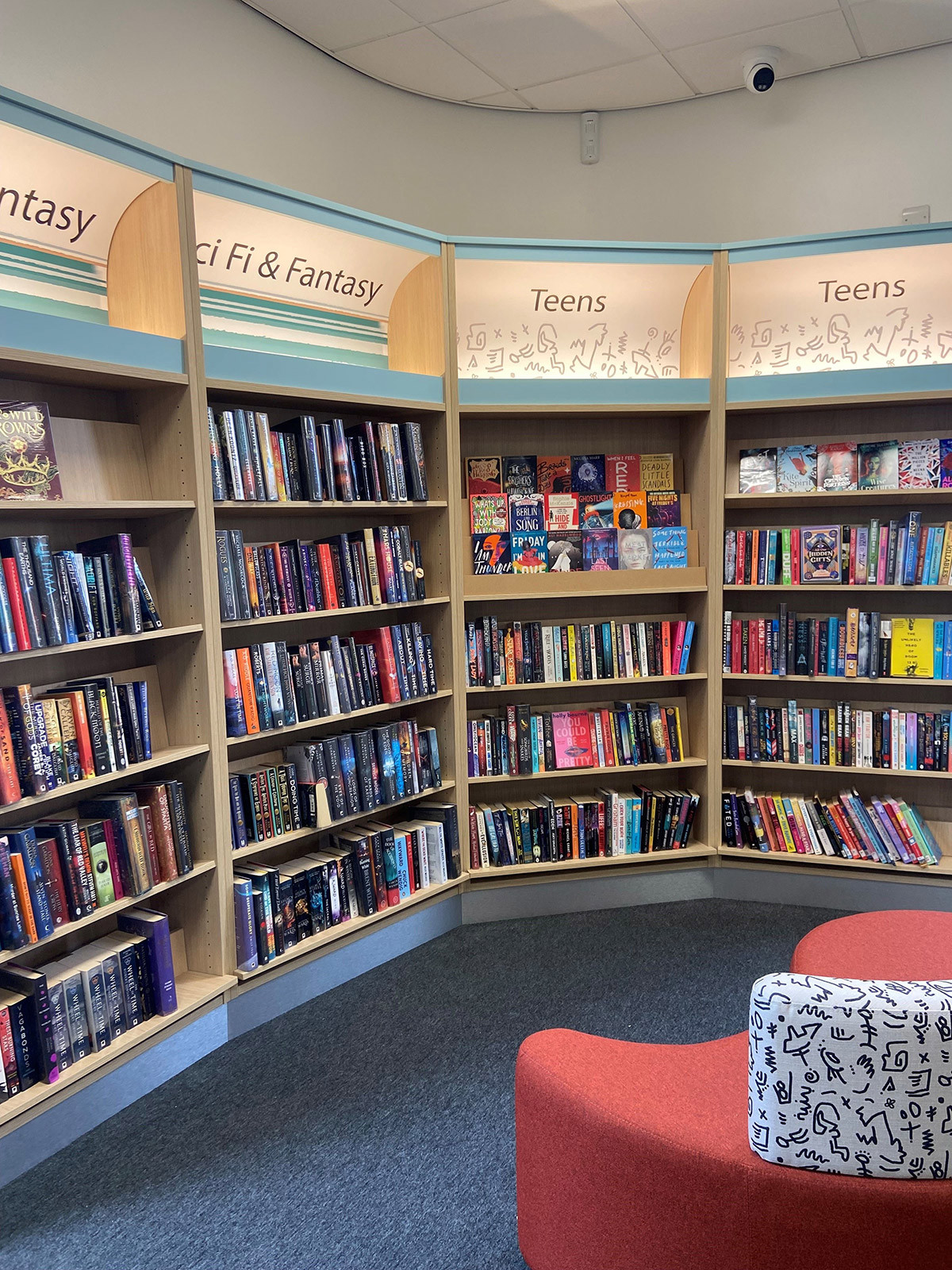 Curved shelving filled with young adult fiction titles and a red upholstered seating area at Blaydon Library