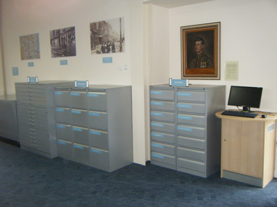 Grey filing cabinets with labelled drawers and a computer station beside historical photographs at Worksop Local Studies