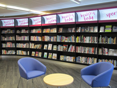 Blue lounge chairs beside a curved bookshelf displaying health-themed titles at Wellington Library