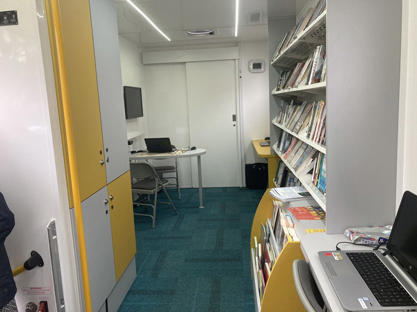 Bright yellow cabinetry and a study table with chairs in a quiet reading space at Leeds Mobile Community Hub