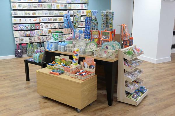 Colourful merchandise displays featuring toys and stationery on wooden tables at Gateshead Library Shop – well-merchandised display