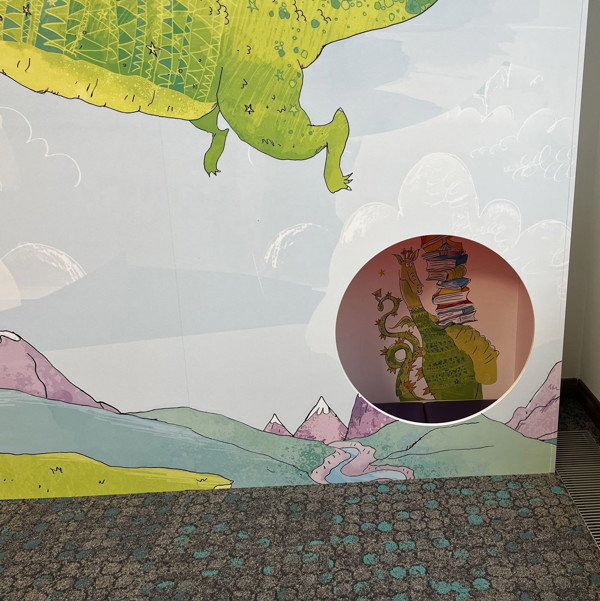 Illustrated dragon and mountain mural with a circular cutout revealing a stack of books at Stoke City Central Library