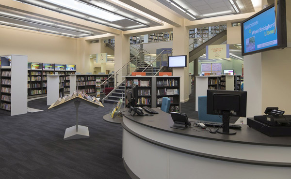 Reception desk with a curved display stand and browsing shelves in the open-plan layout at West Bridgford Library