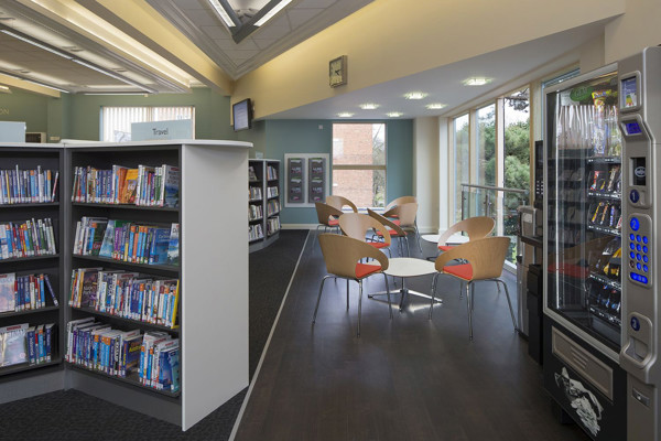 Curved wooden chairs with orange upholstery around a circular table in a reading lounge at West Bridgford Library