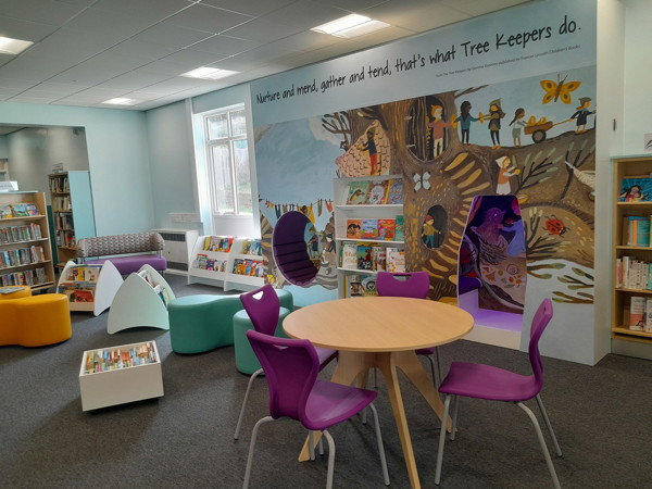 Purple and green chairs around a circular table in a children's reading area with a mural at Birtley Library
