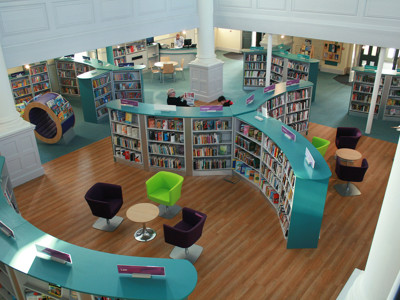 Curved turquoise shelving and purple lounge chairs in a public library browsing area at St Aubyn Library Church